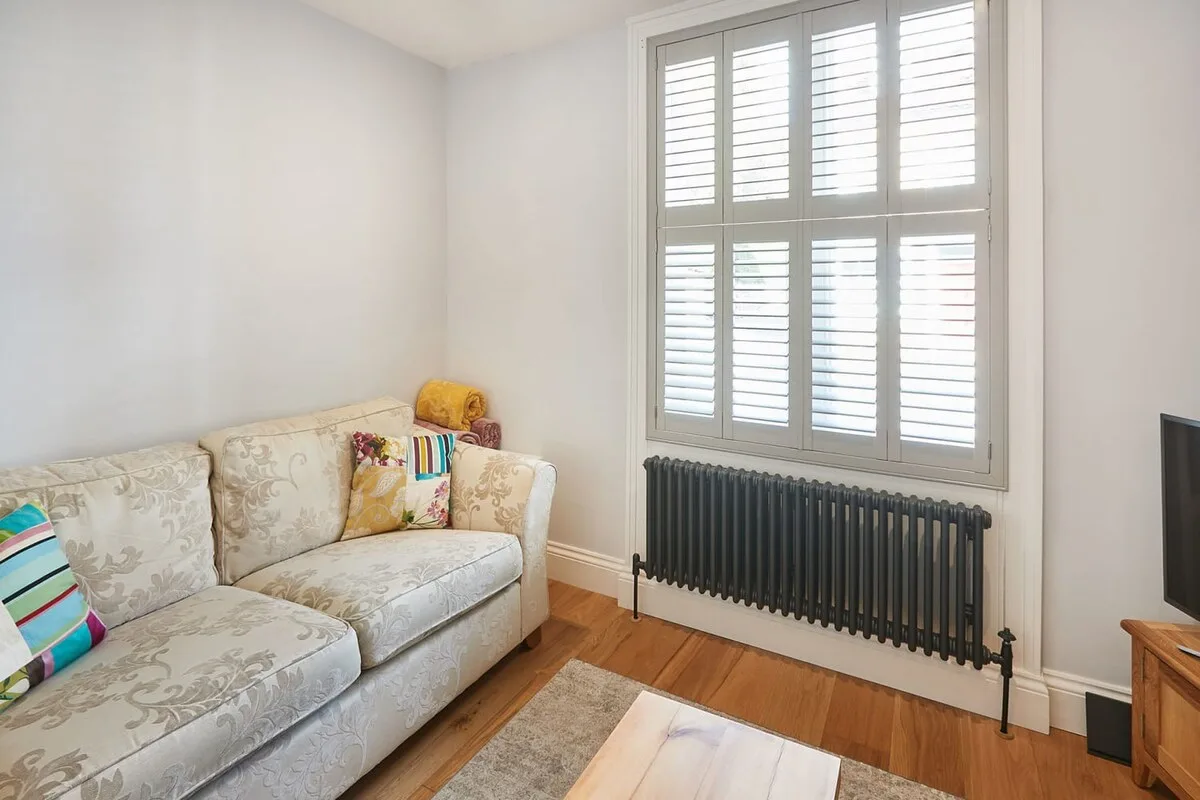 Una sala de estar con asientos estampados junto a una ventana con contraventanas.