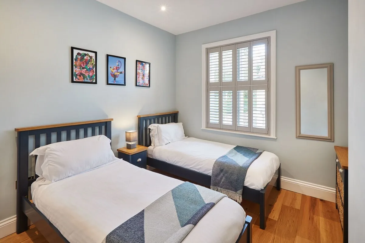 Un dormitorio con dos camas, cuadros enmarcados y una ventana con contraventanas.