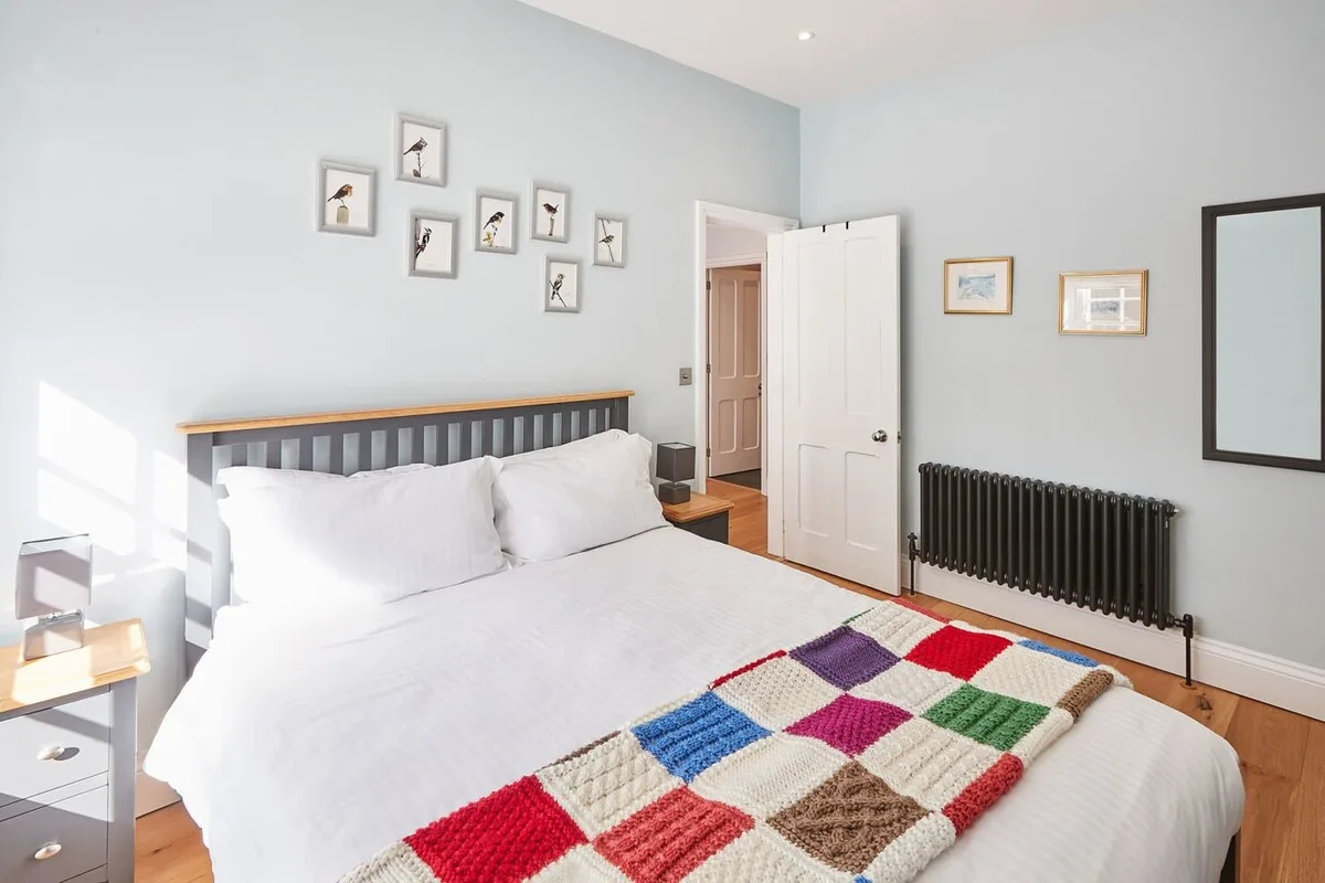Un dormitorio luminoso con una cama tendida y una colorida manta de retazos.