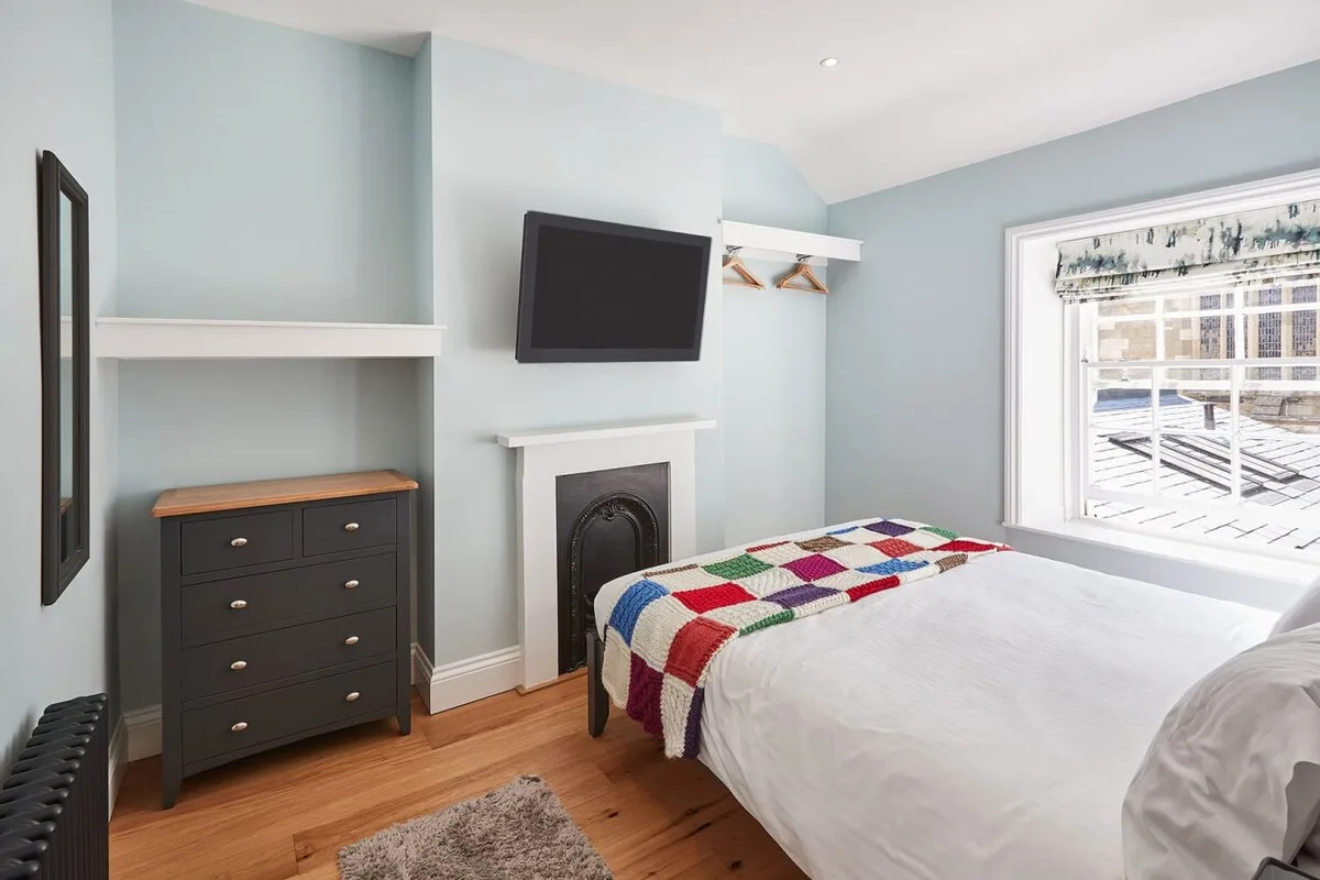Un dormitorio con cama, cómoda, televisor y chimenea.
