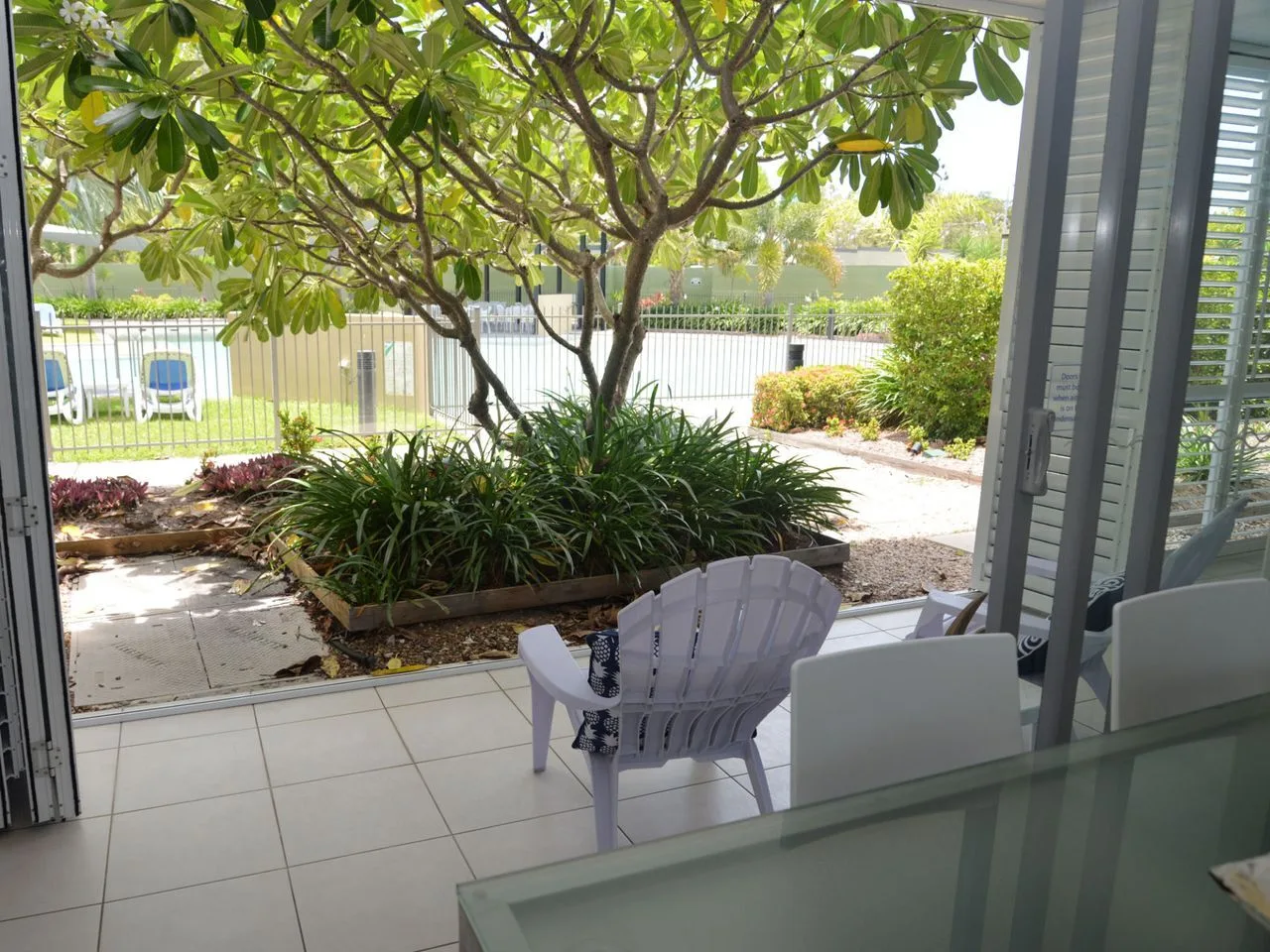 A tiled patio with outdoor seating overlooks a leafy garden and fenced lawn.