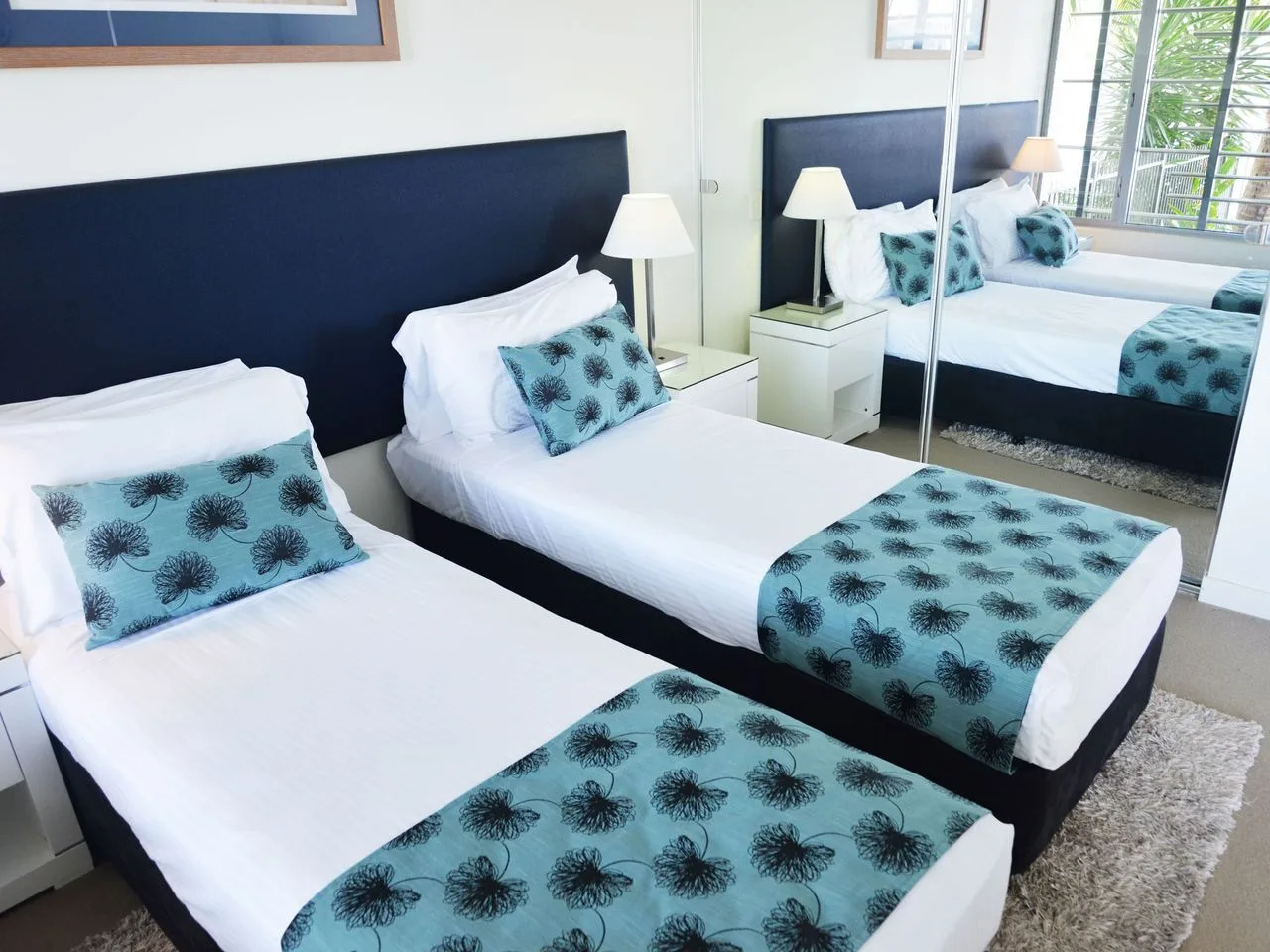 A bedroom with two beds dressed in white and turquoise bedding.