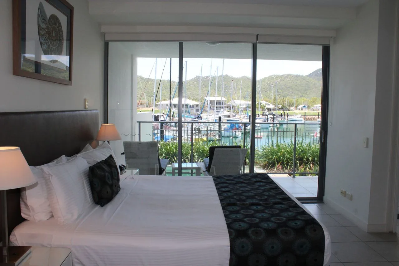 A bedroom with a bed facing large windows overlooking a marina.