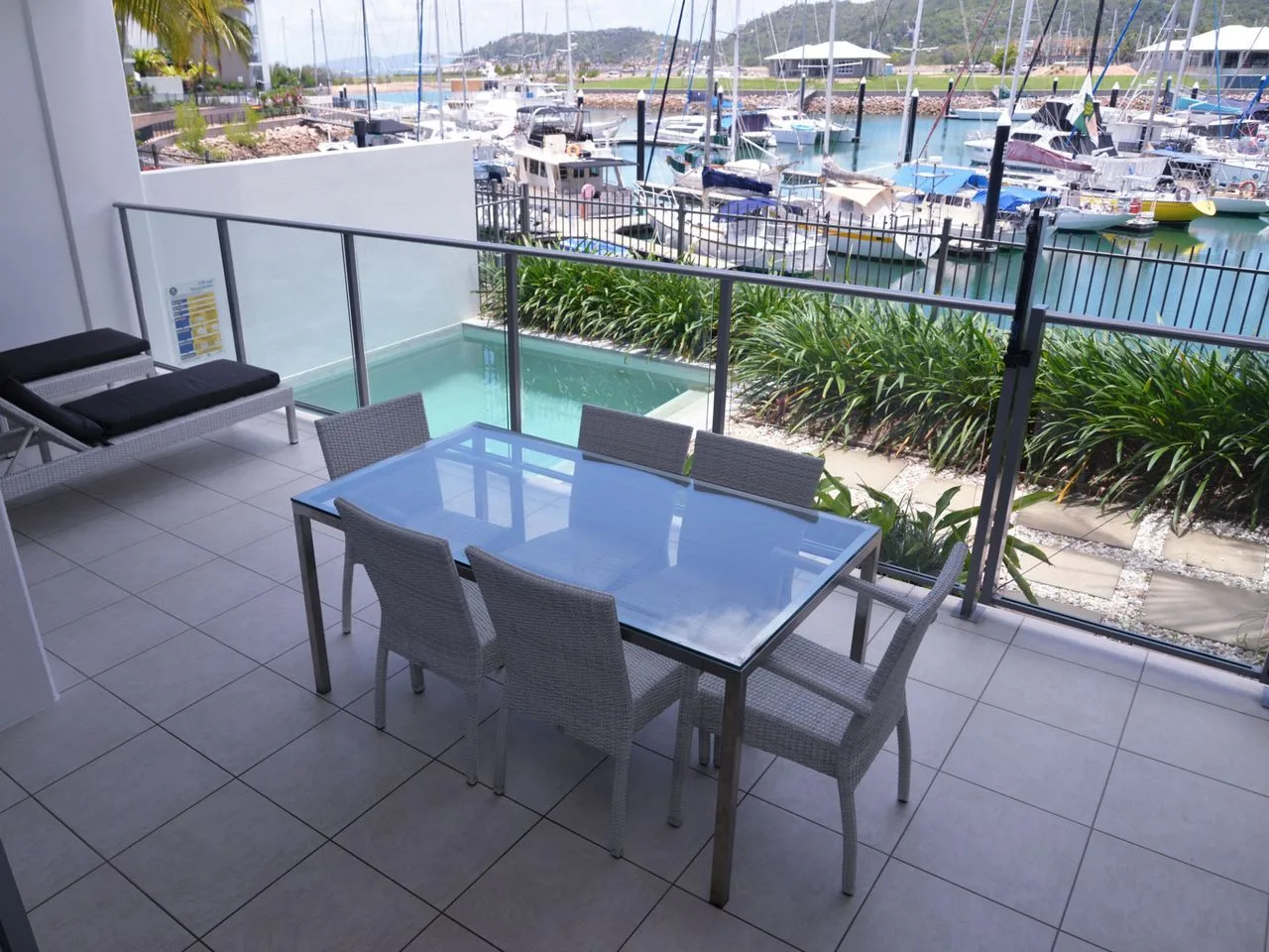A waterfront patio with a glass dining table overlooks a marina.