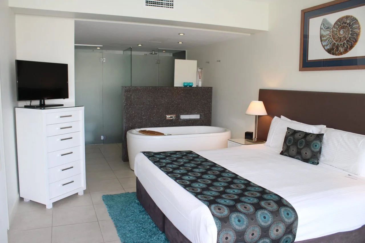 A bedroom with a white bed, patterned runner, and television on a dresser.