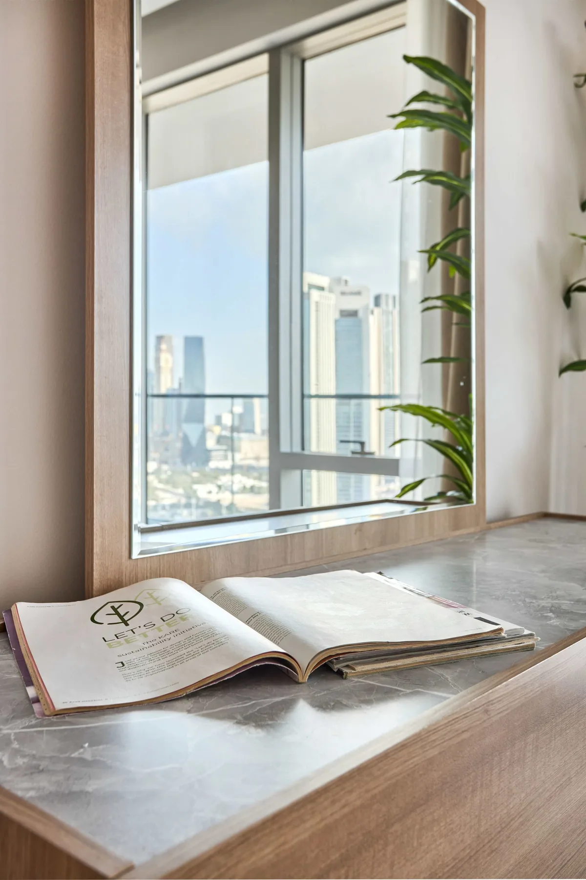 An open book rests on a table beside a large window overlooking city buildings.