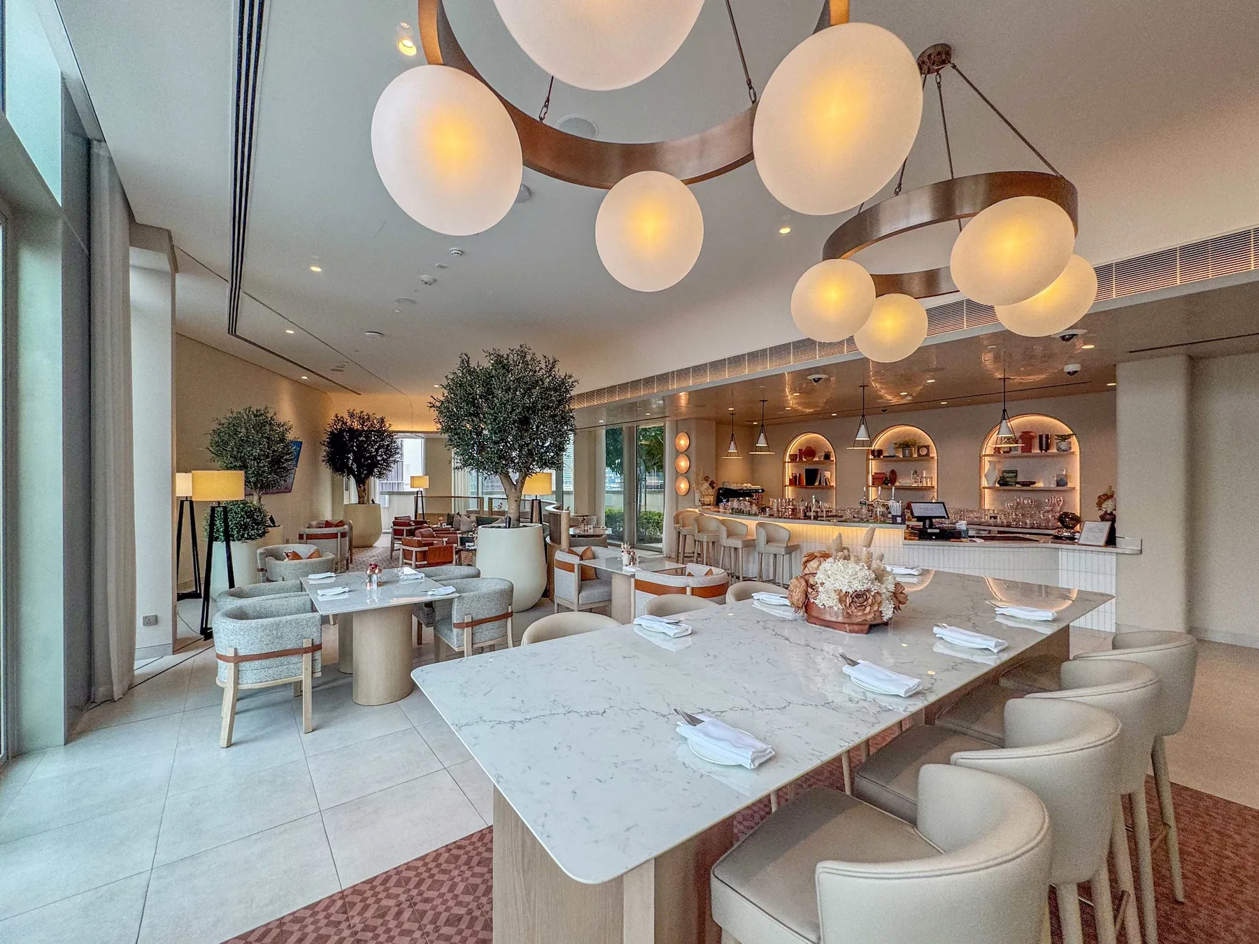 A bright dining area with a long table, upholstered seating, and pendant lights.