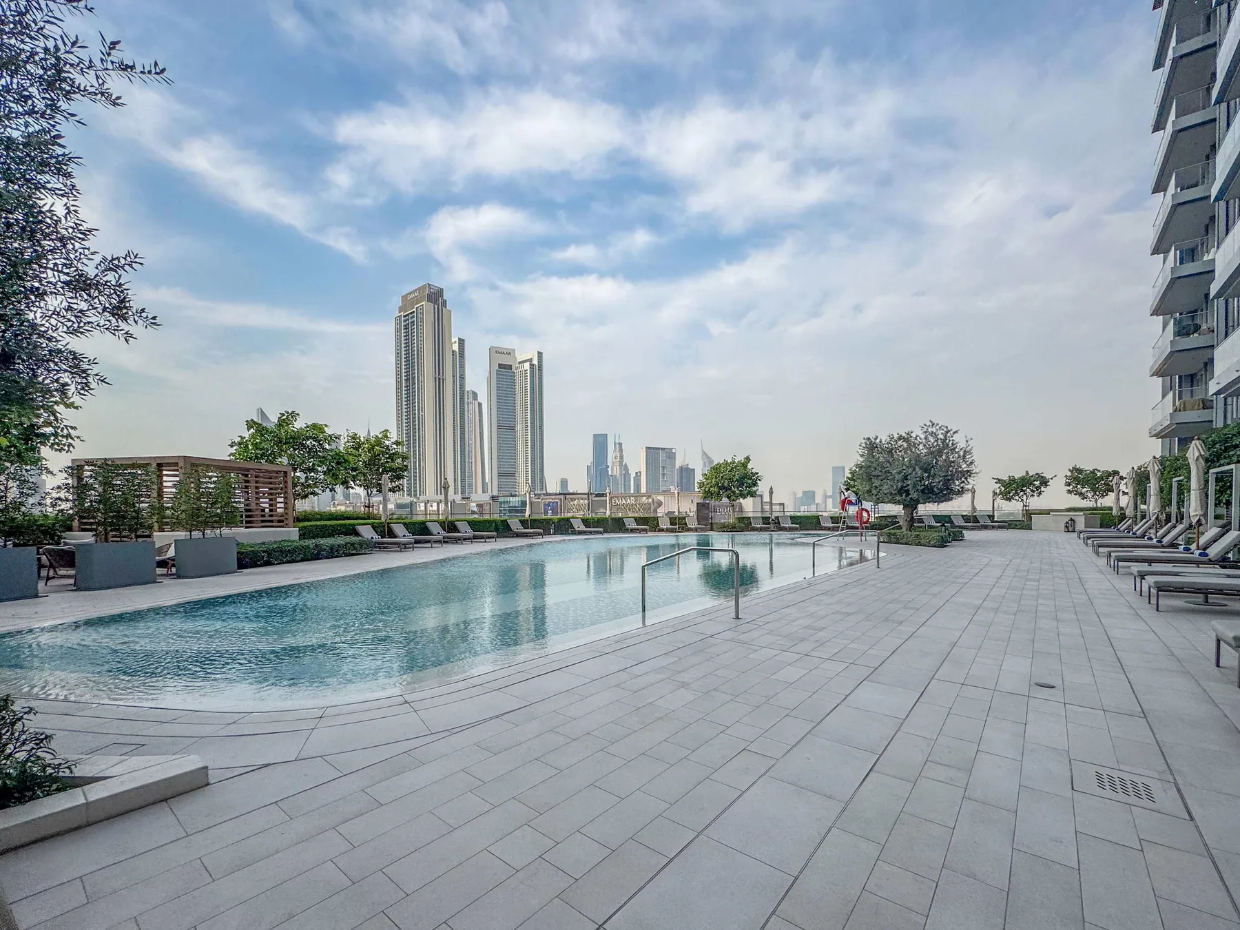 An outdoor swimming pool and paved deck overlook a distant city skyline.