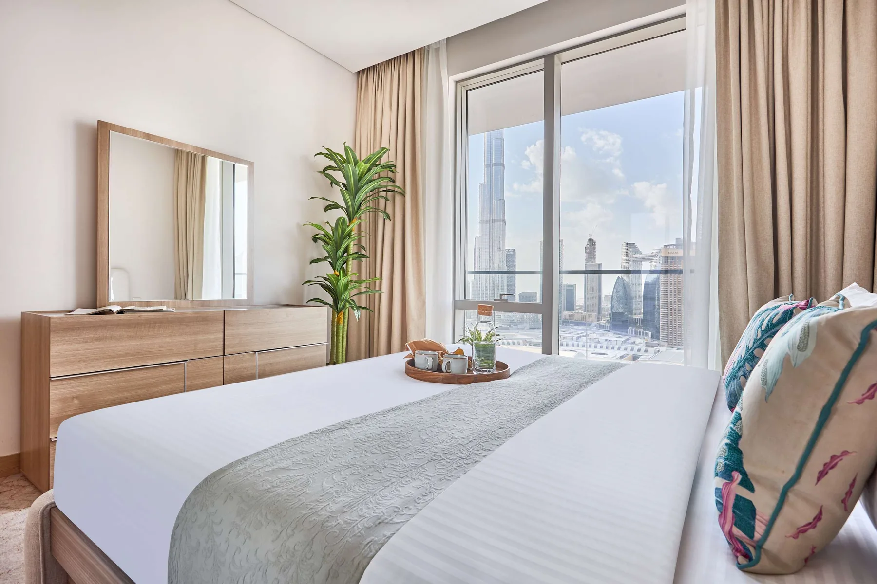 A bright bedroom with a neatly made bed and a large window overlooking the city.