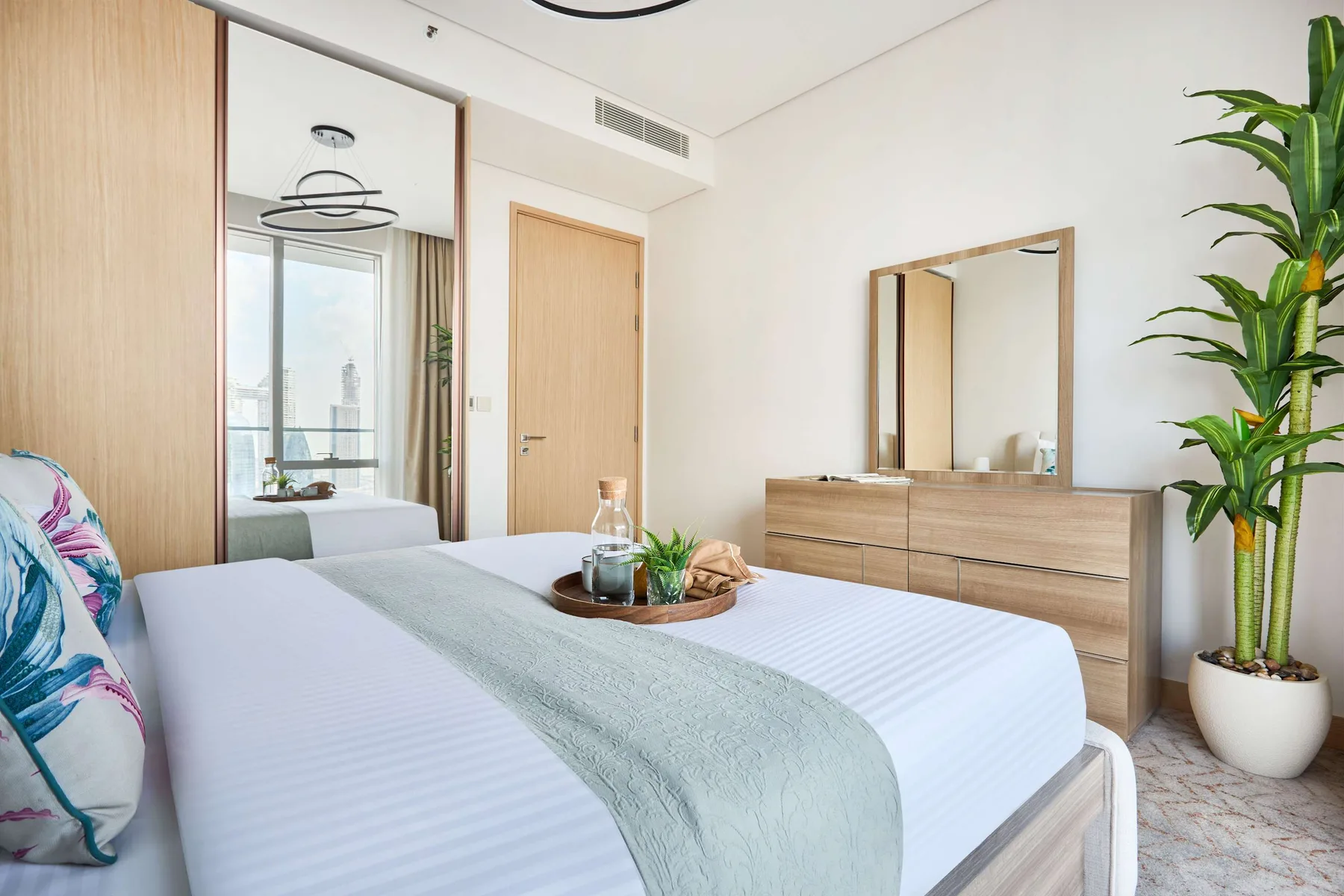 A bright bedroom with a neatly made bed and a large mirror above a dresser.