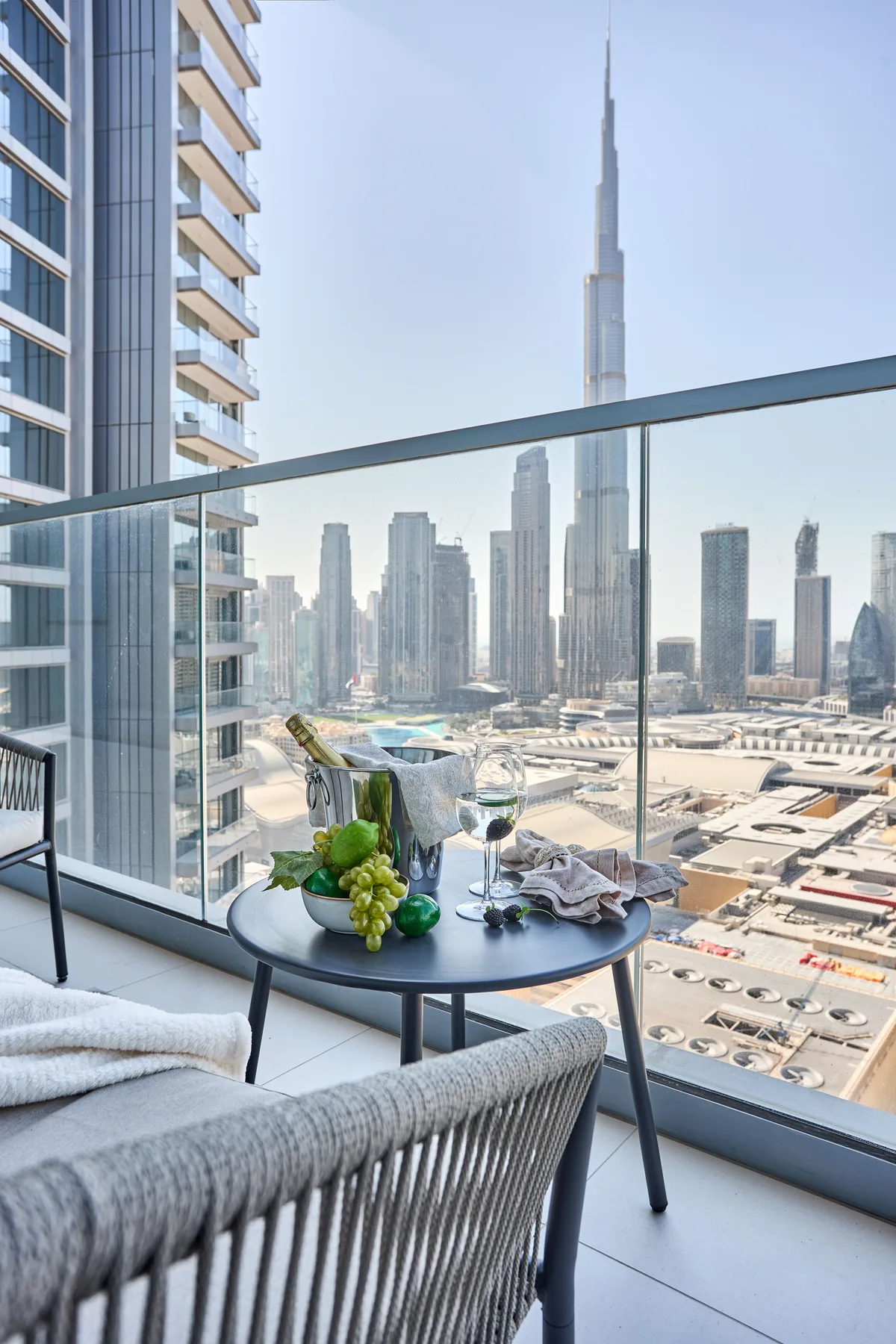 A balcony seating area overlooks a city skyline, with fruit and drinks on a table.
