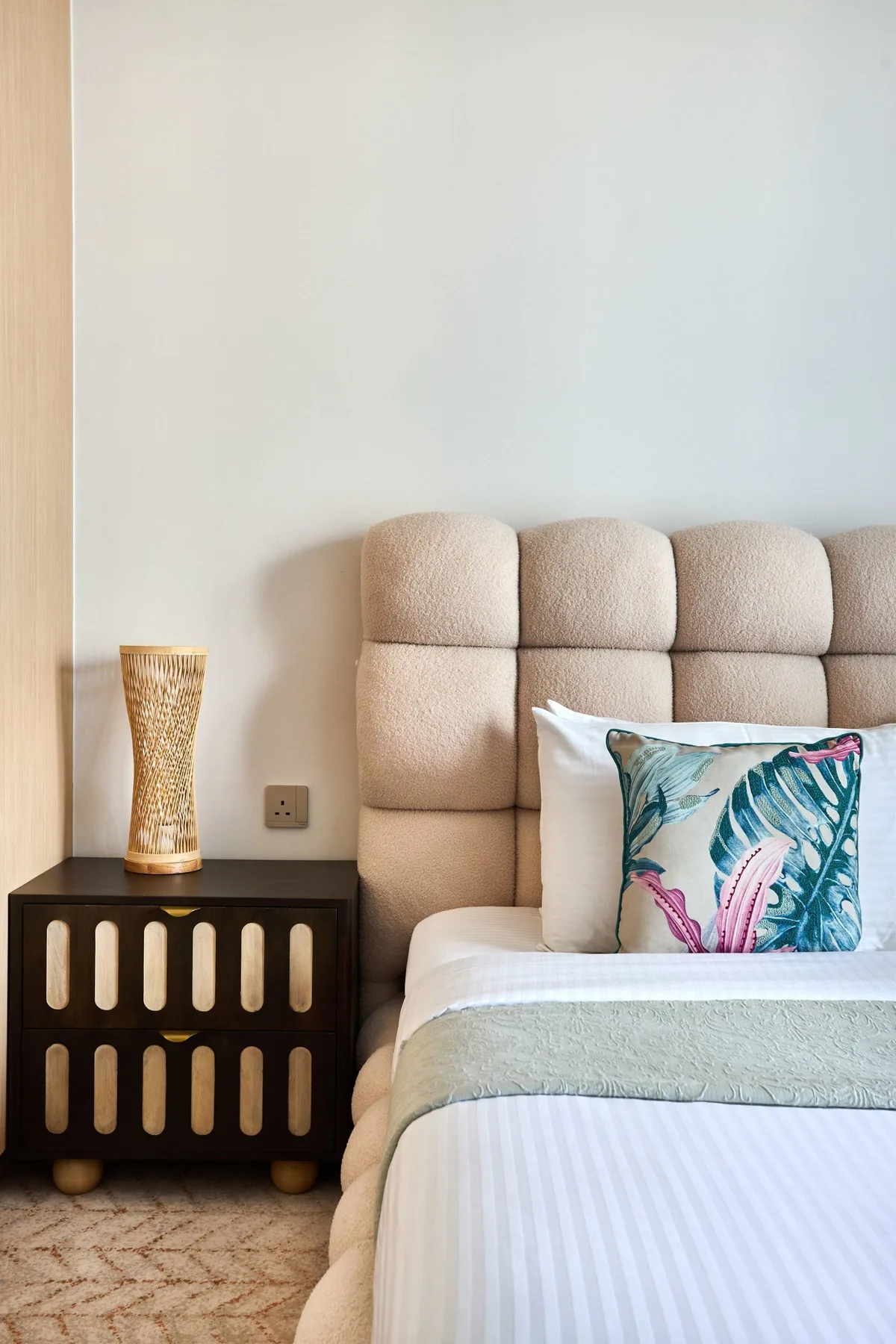 A bedroom with a bed, padded headboard, and colorful decorative pillow.