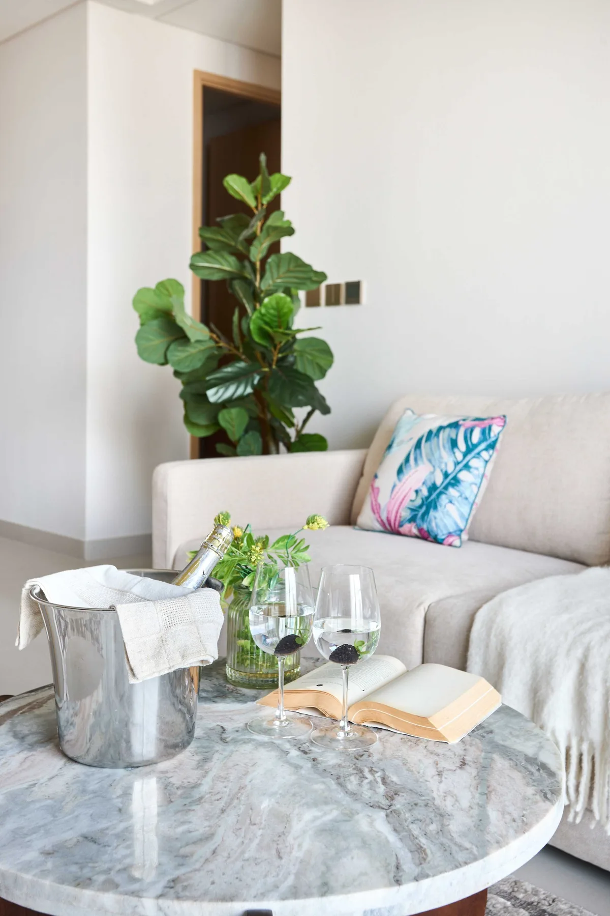 A bright living room with seating, a round coffee table, and a leafy plant.