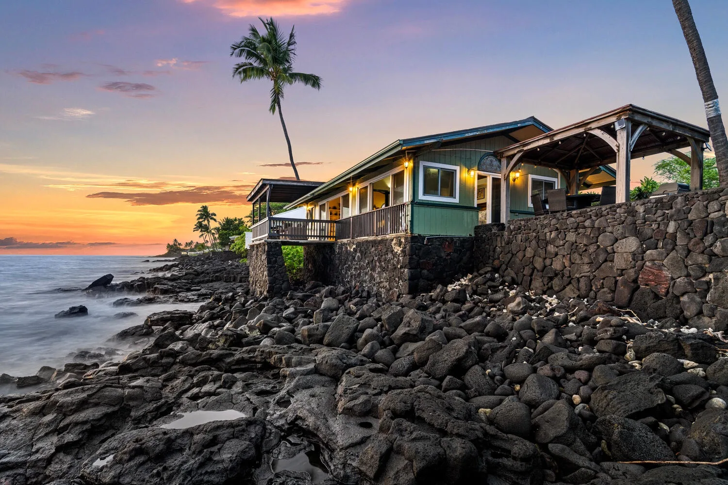 Una casa costera se alza sobre una orilla rocosa al atardecer.