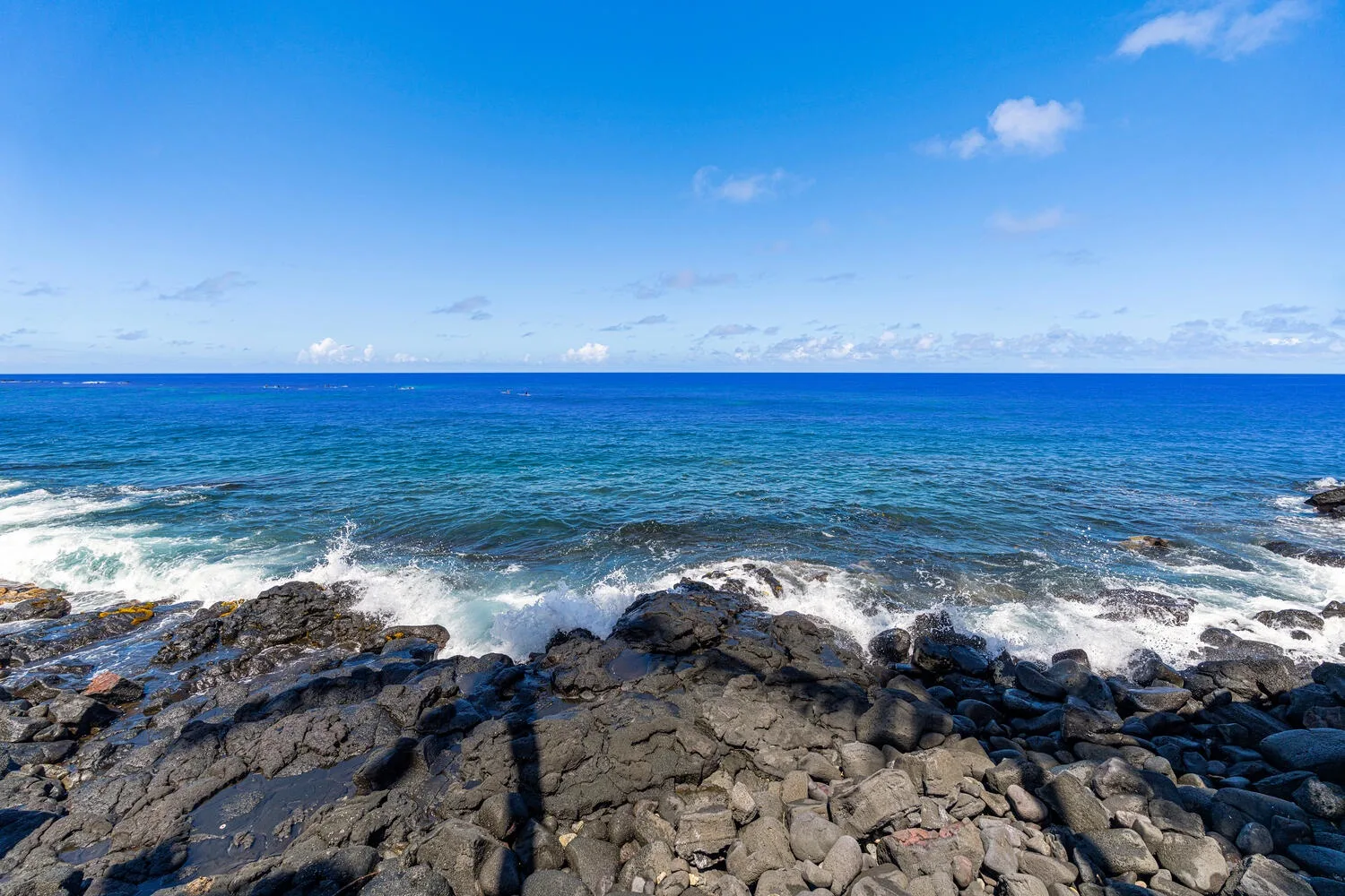 Las olas del océano azul rompen contra una costa rocosa bajo un cielo despejado.