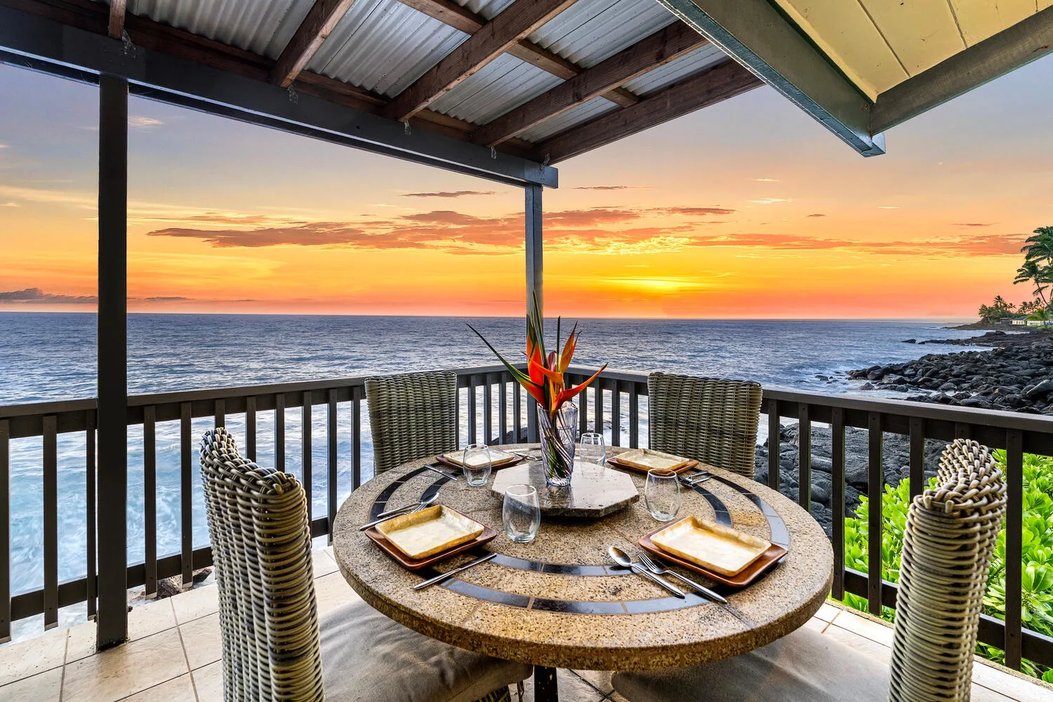 Una zona de comedor al aire libre mira al océano al atardecer.