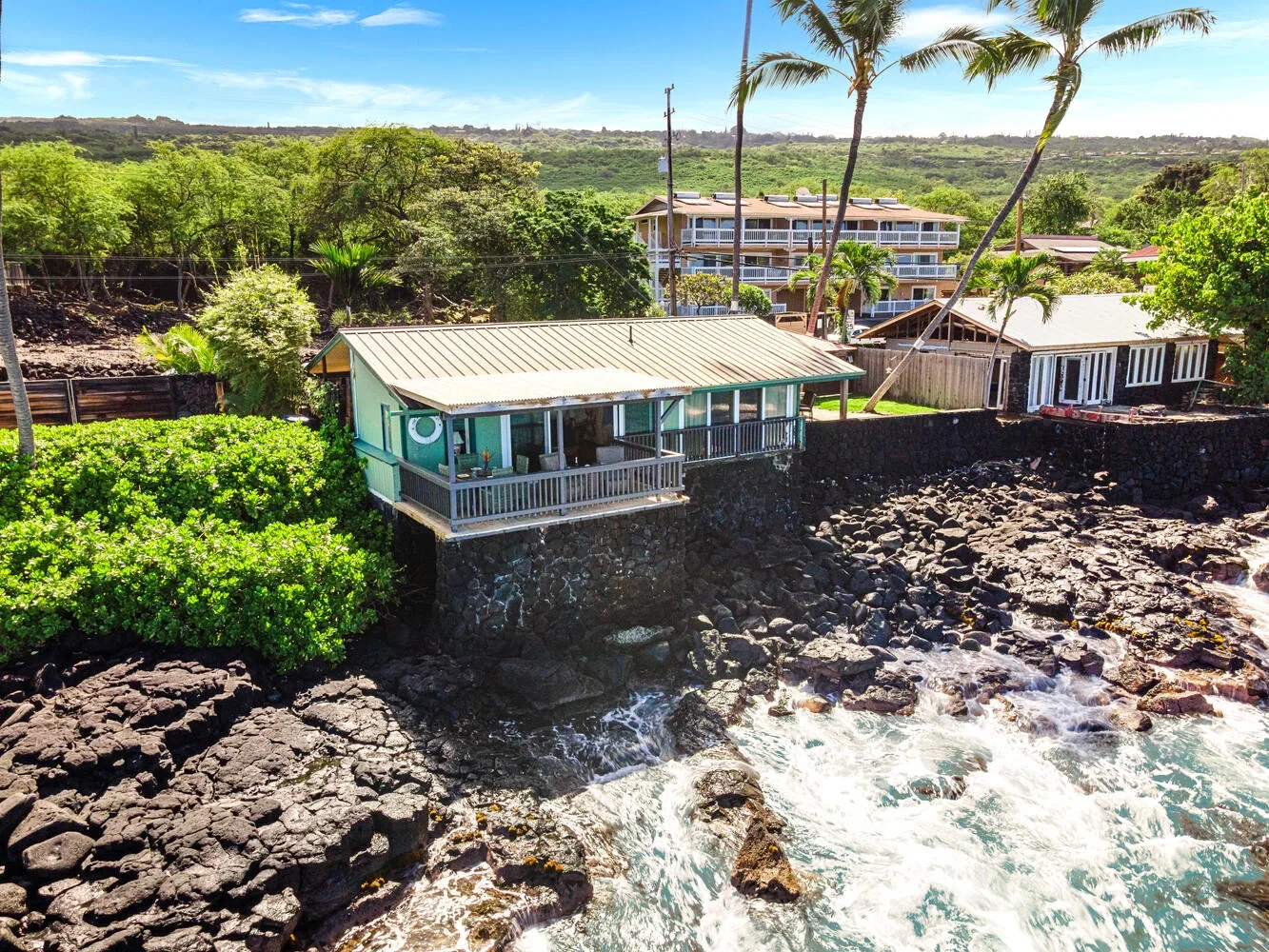 Un edificio costero con una terraza cubierta se alza junto a una costa rocosa y olas.