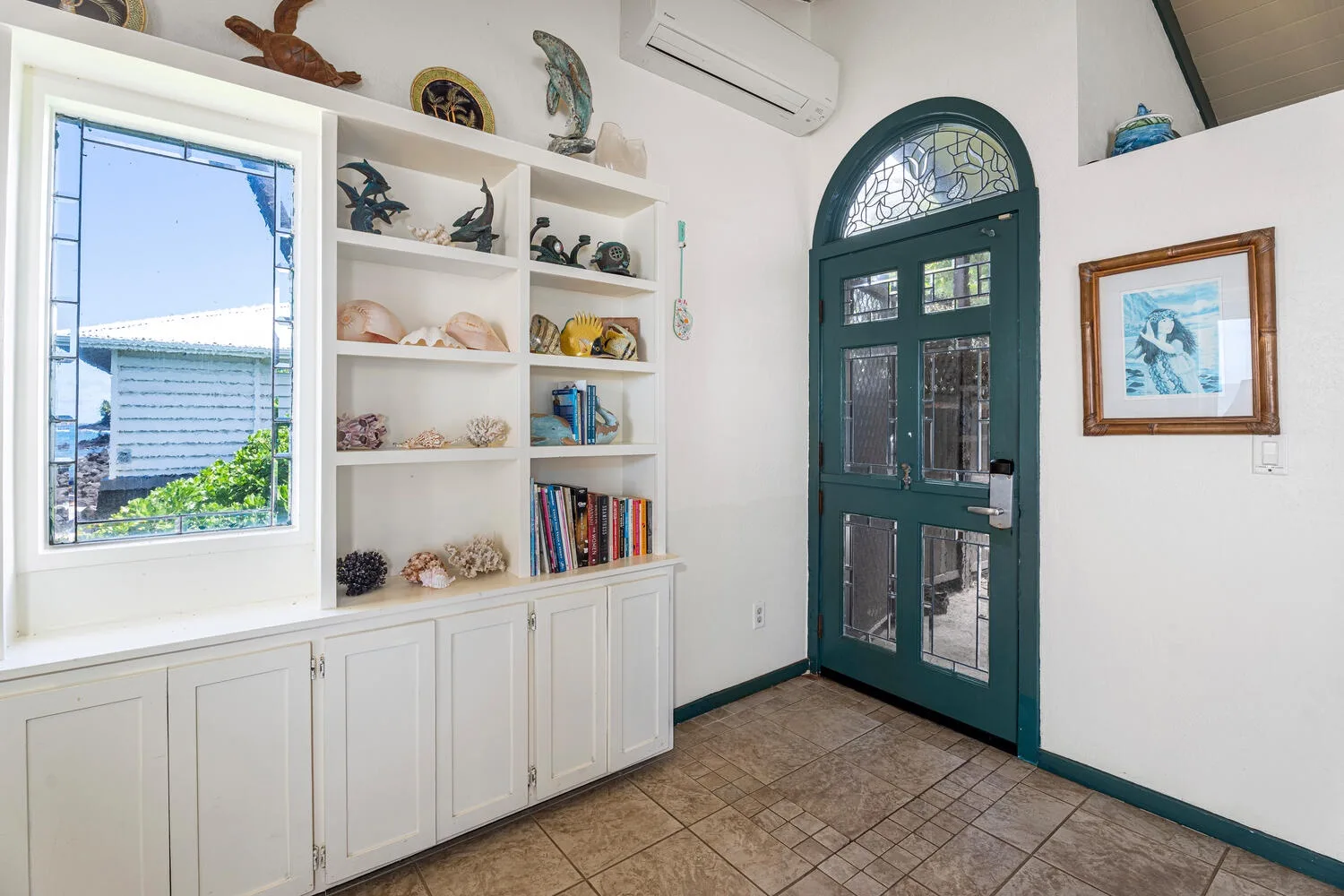 Una habitación luminosa con estantes empotrados, una ventana y una puerta verde oscura.