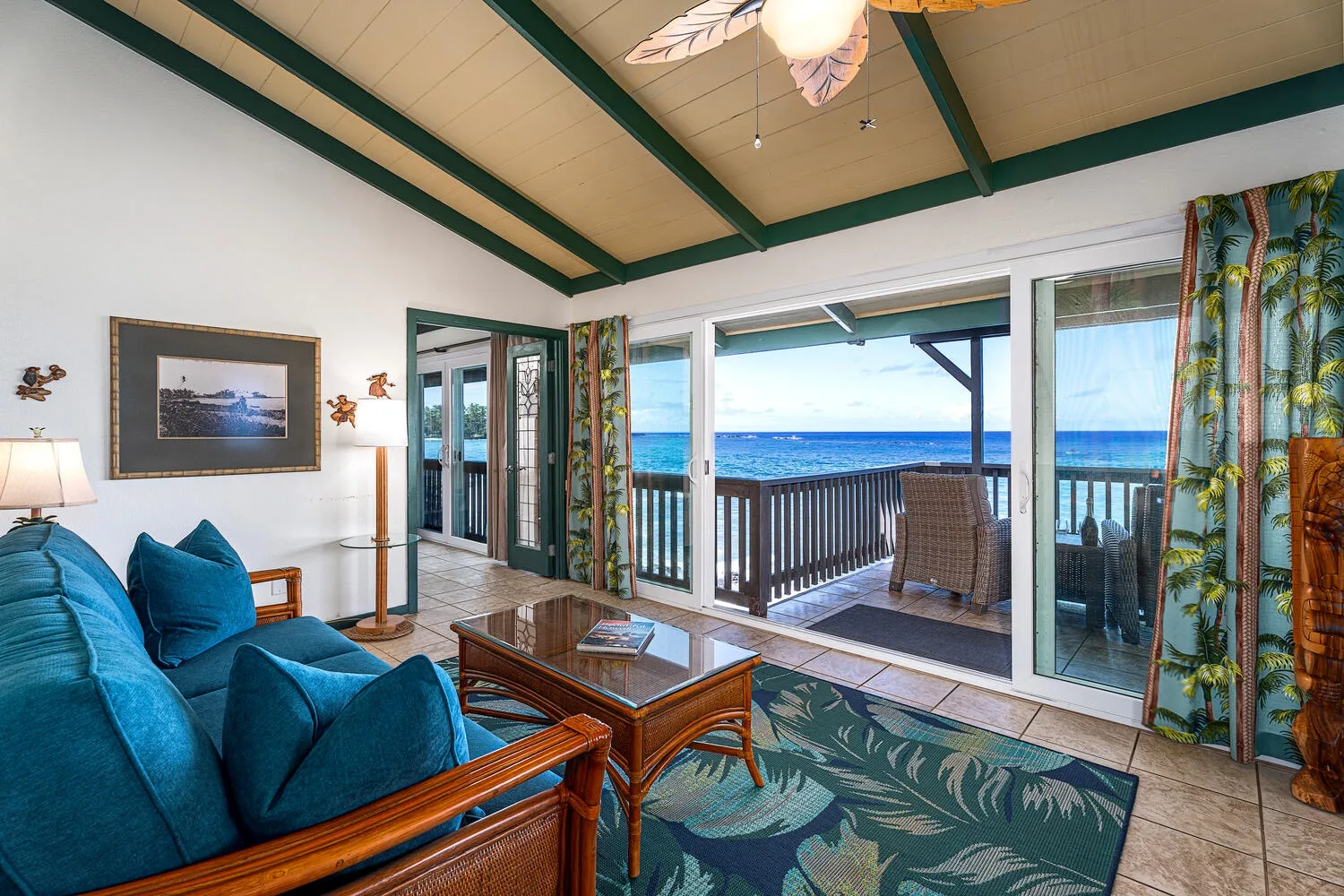 Sala de estar con asientos azules, una mesa de centro y puertas corredizas con vista al mar.