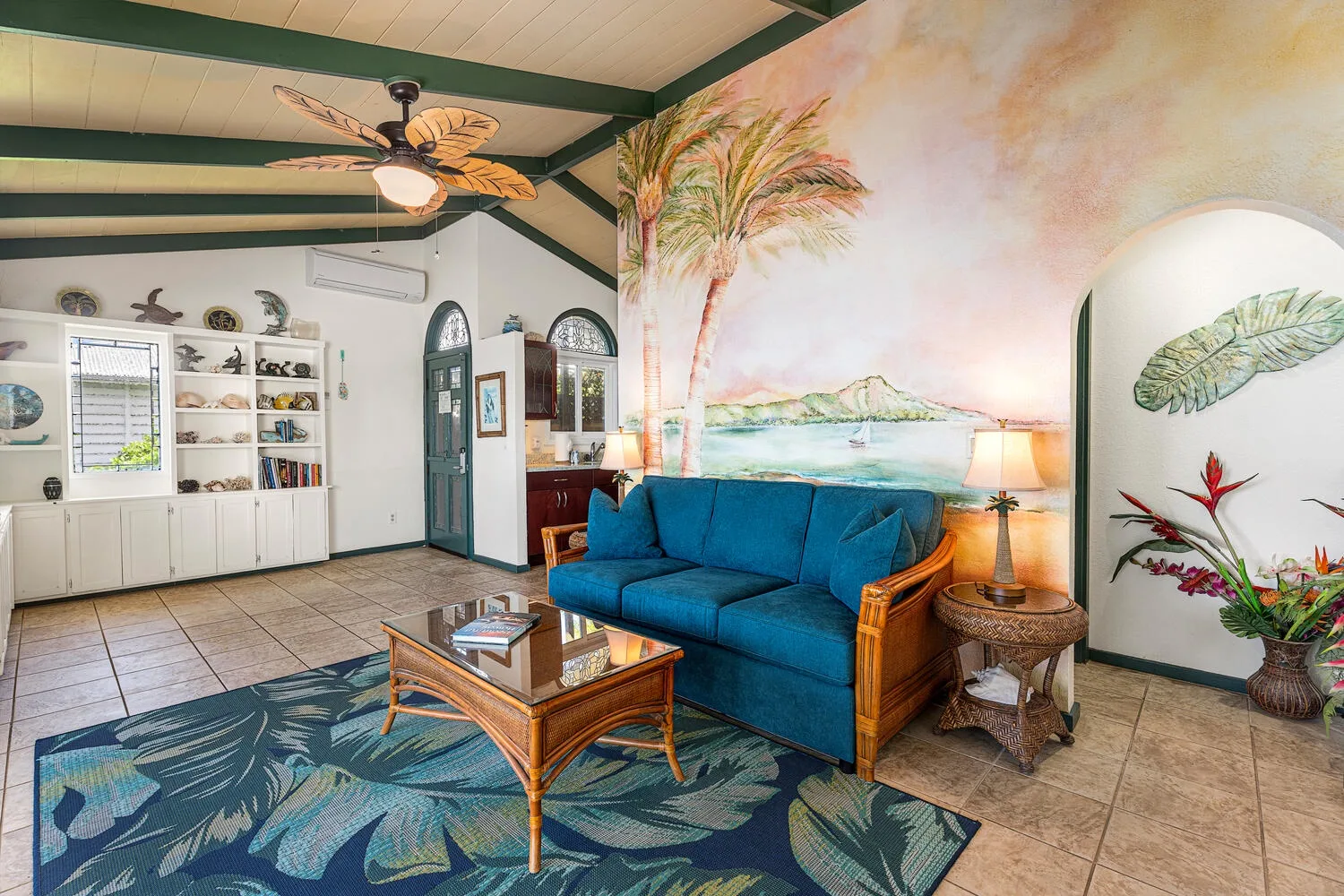 Una sala colorida presenta asientos azules, una mesa con tapa de vidrio y un mural tropical.