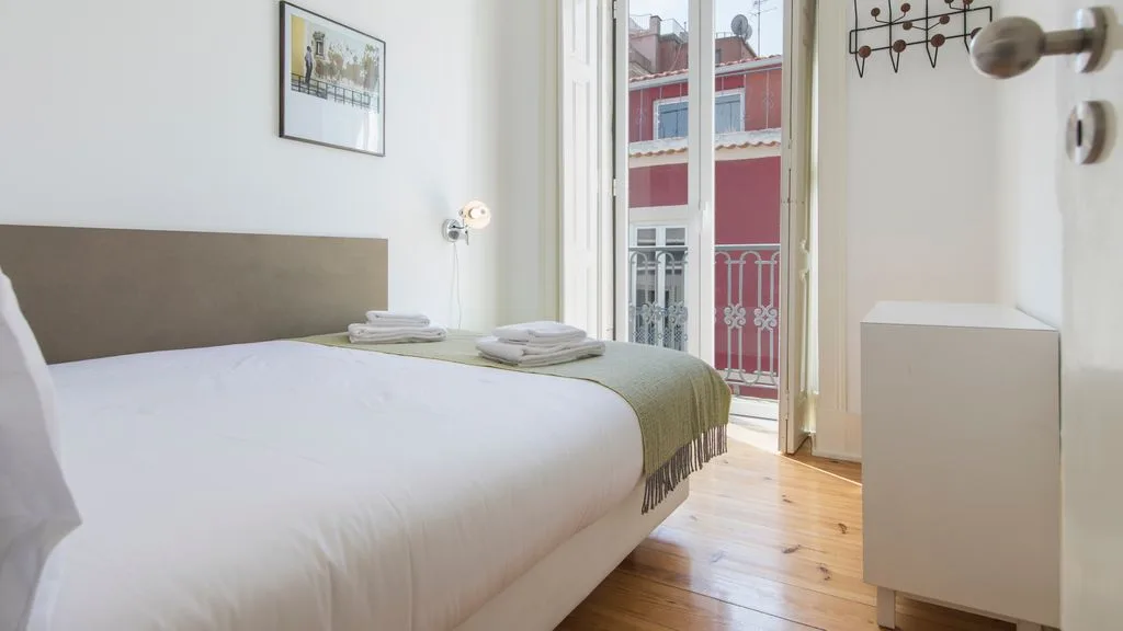 Un dormitorio luminoso con una cama bien tendida junto a ventanas altas.