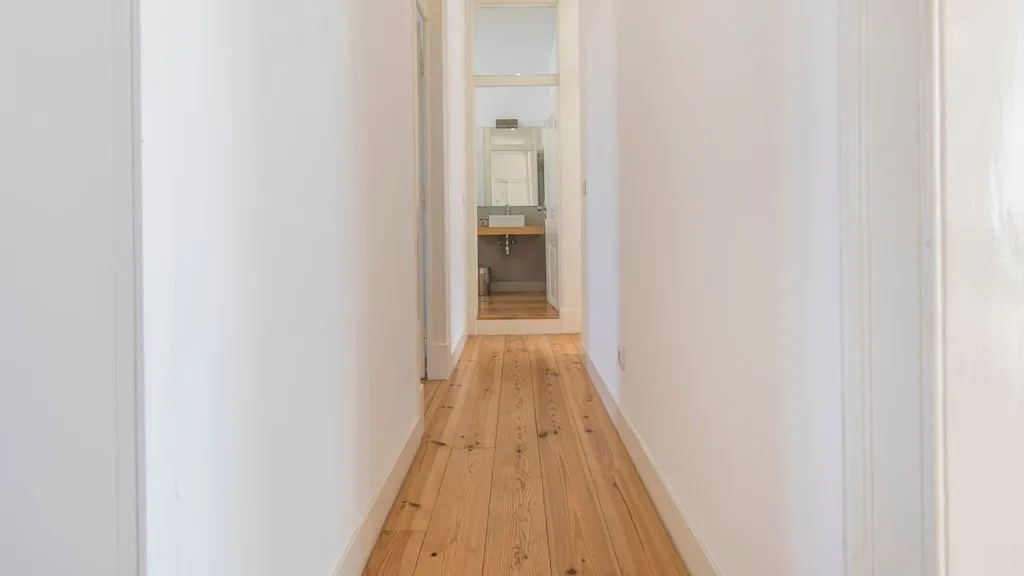 Un pasillo estrecho con suelo de madera conduce a una habitación al fondo.