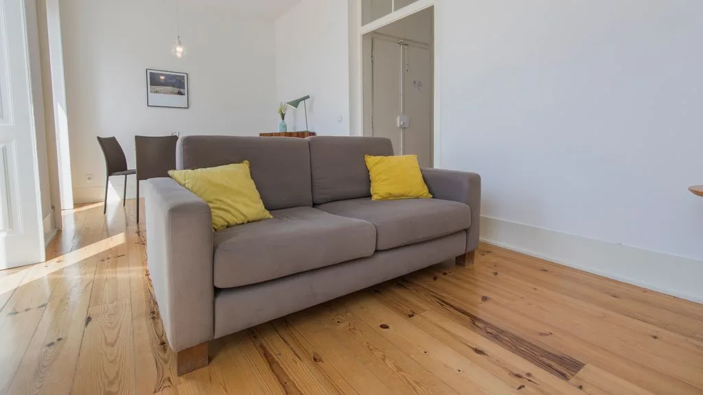 Una sala de estar con un sofá gris y suelo de madera.