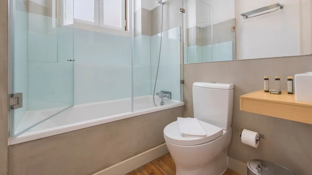 Un baño luminoso con bañera, inodoro y suelo de madera.