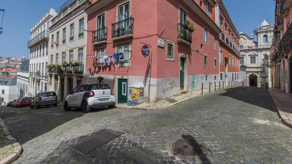 Una calle empedrada pasa entre edificios coloridos con coches estacionados.
