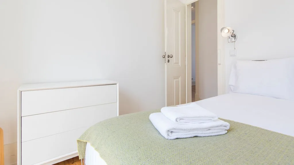 Un dormitorio con una cama, toallas dobladas y una cómoda blanca.