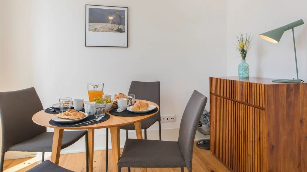 Comedor con una mesa redonda puesta con platos y bebidas junto a un aparador de madera.