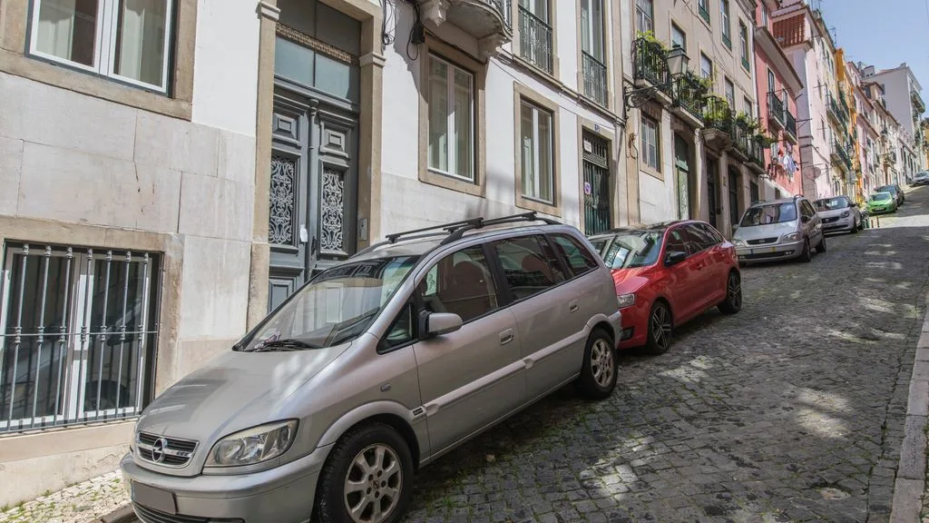Una calle urbana adoquinada con coches estacionados y edificios de varias plantas.