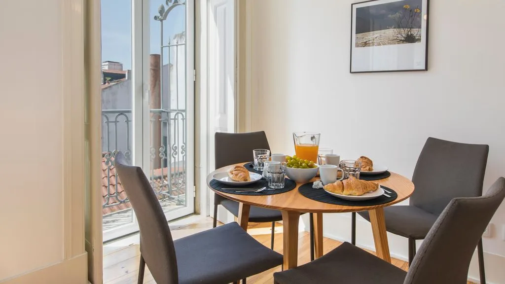 Comedor con una mesa redonda puesta con platos y comida junto a ventanas altas.