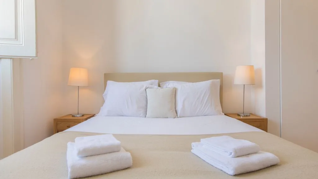 Un dormitorio luminoso con una cama, ropa de cama blanca y lámparas de noche.