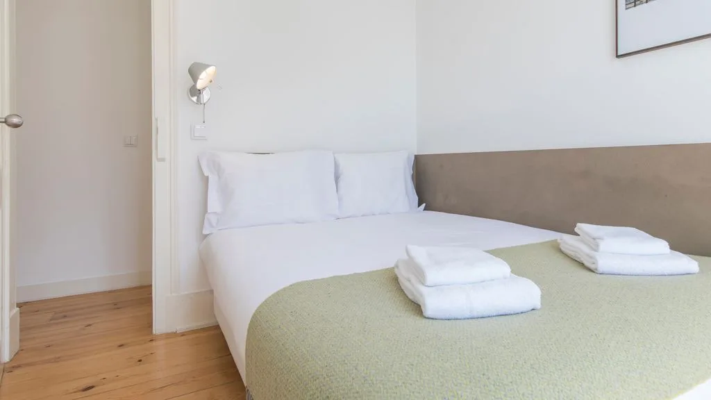 Un dormitorio con una cama cubierta por una manta verde claro y toallas dobladas.