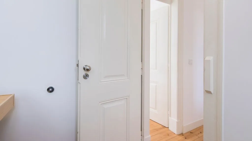 Un pasillo interior luminoso con puertas blancas abiertas y suelo de madera clara.