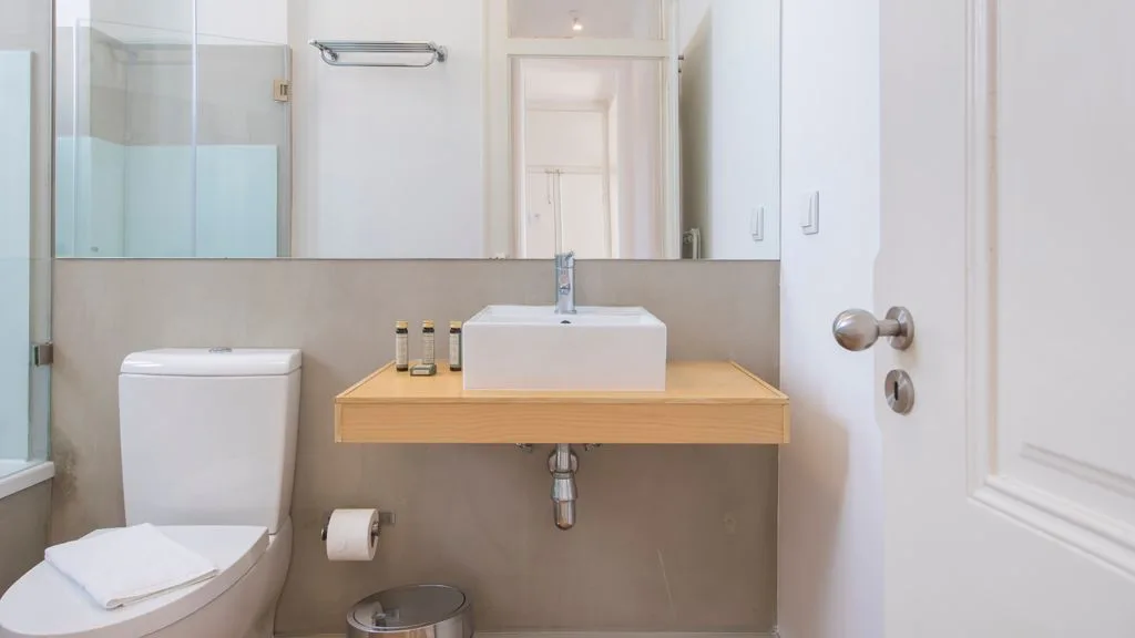Un baño con lavabo suspendido, inodoro y un espejo grande.