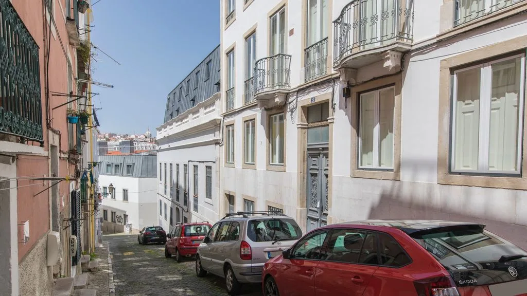 Una calle urbana estrecha bordeada de edificios y coches aparcados.