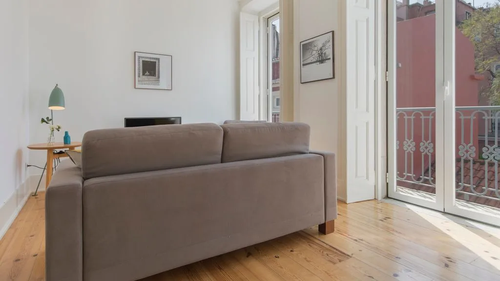 Un salón luminoso con un sofá frente a ventanales y un balcón.
