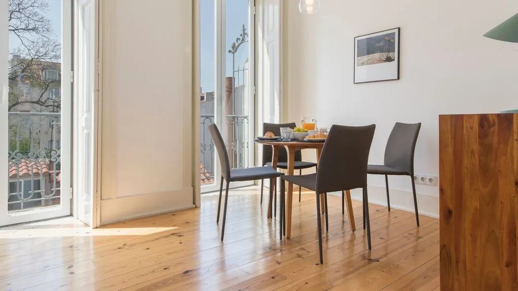 Un comedor luminoso con una mesa y sillas junto a ventanales altos.