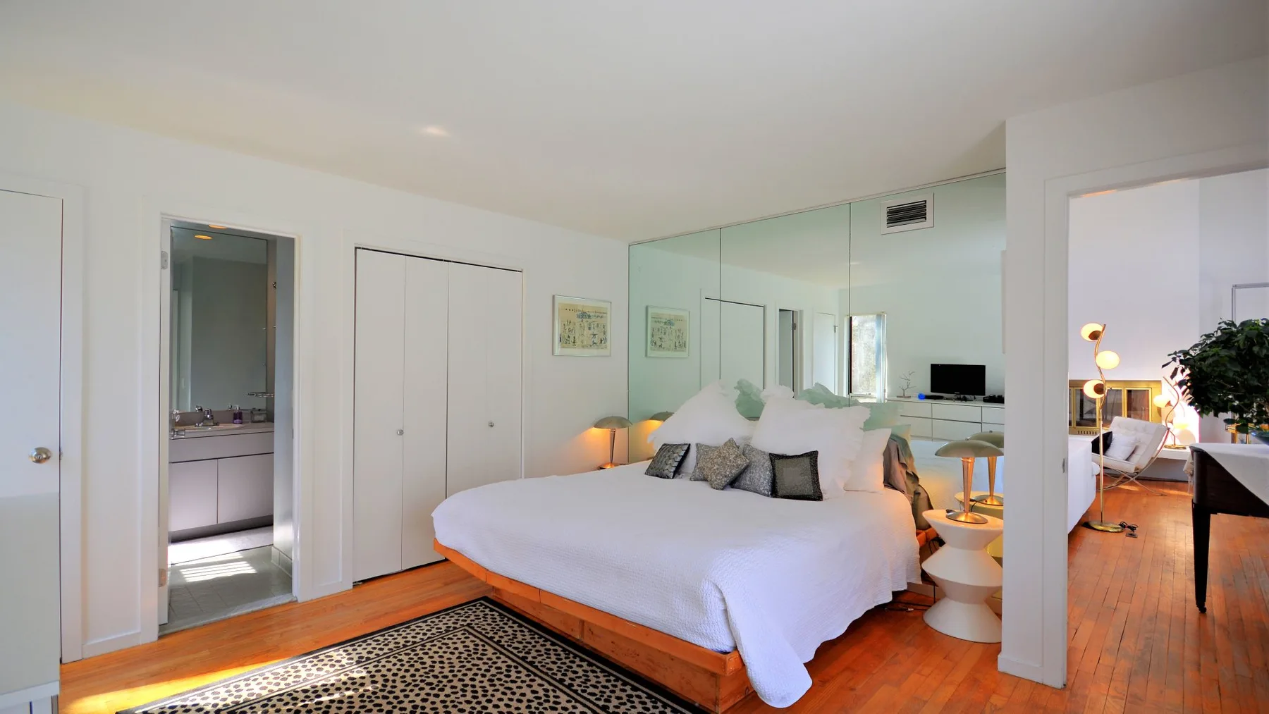 A bedroom with a large bed and mirrored wall.