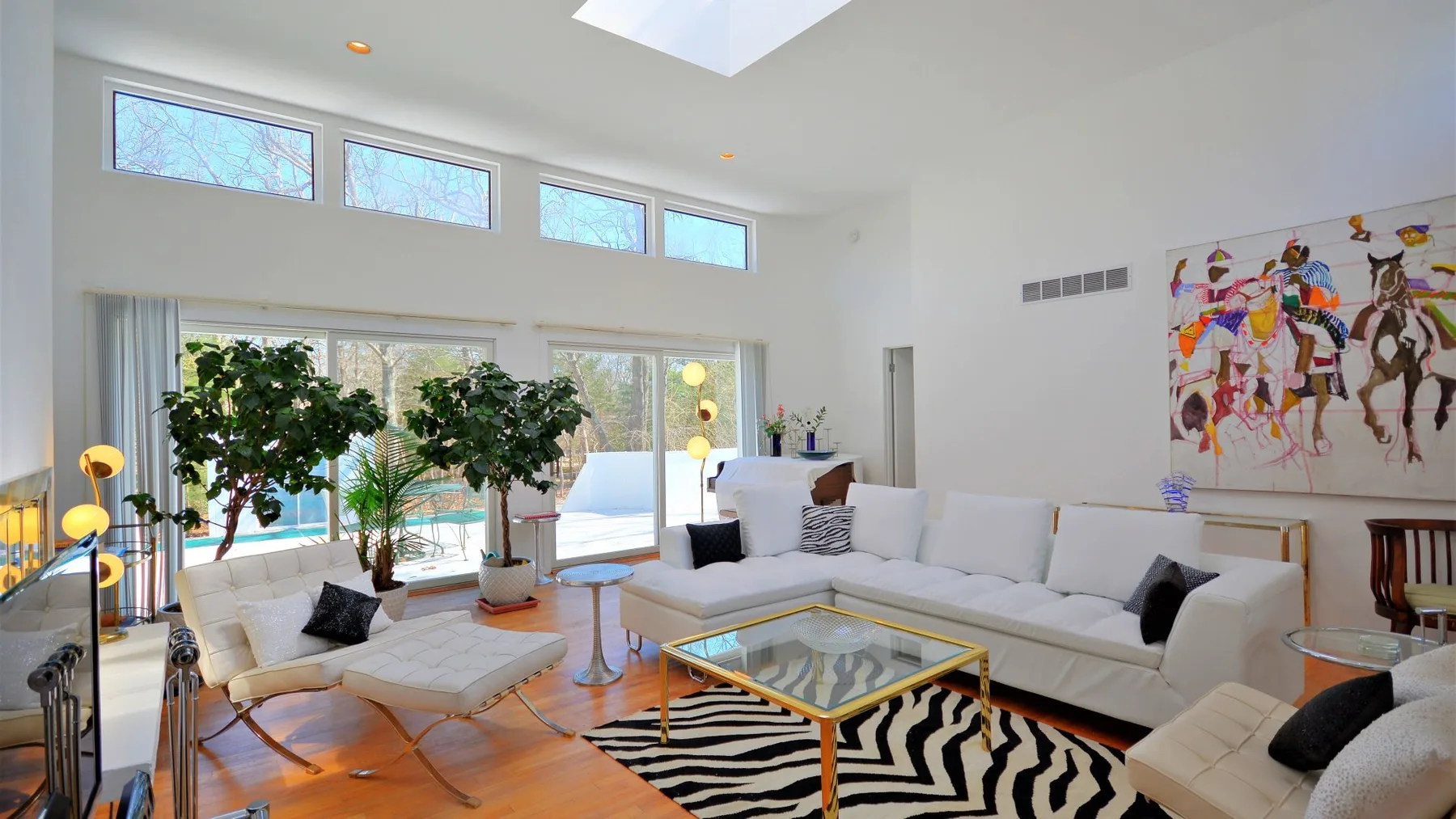 A bright living room with seating around a glass coffee table and large windows.