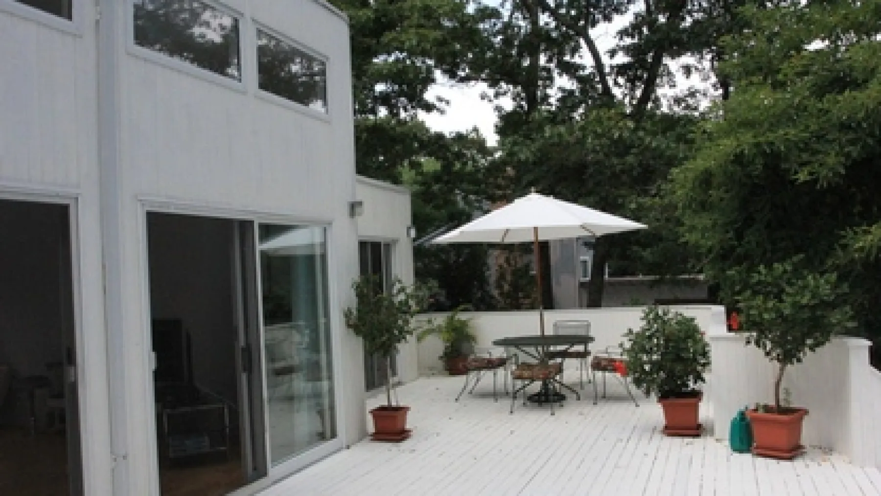An outdoor patio with a dining table and chairs beside a white building.