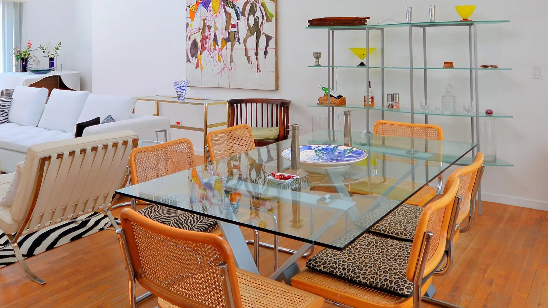 A dining area with a glass table and orange seating beside a white sofa.