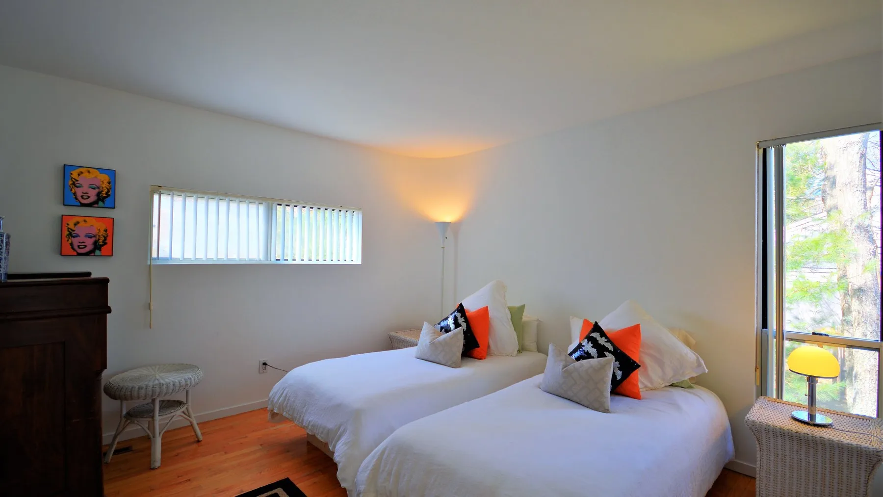 A bright bedroom with two white beds and colorful accent pillows.