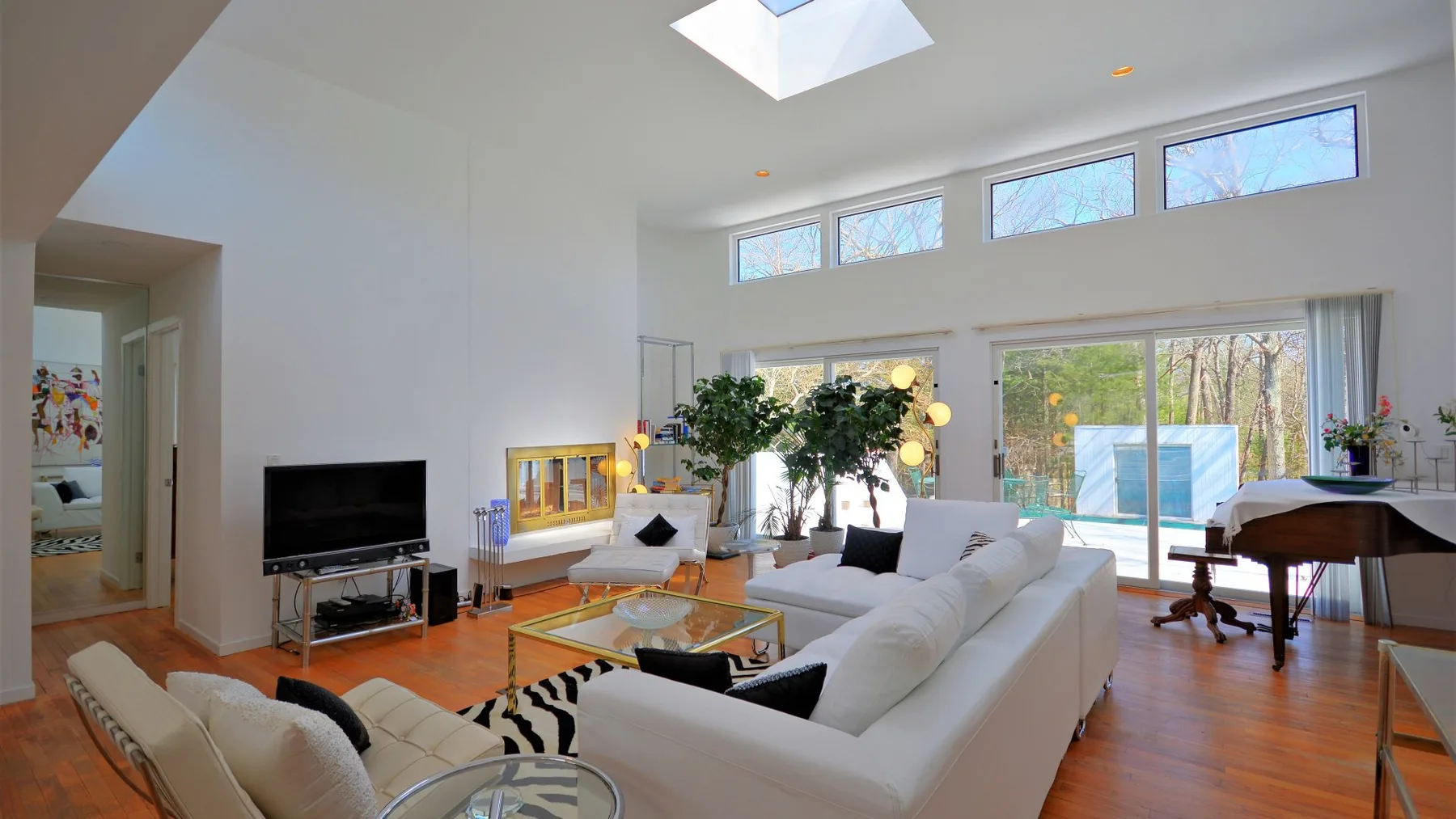 A bright living room with white seating, a glass coffee table, and large windows.