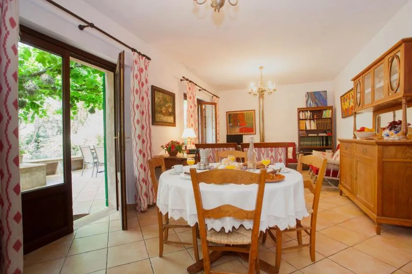 A dining room with a round table set beside large windows opening onto greenery.