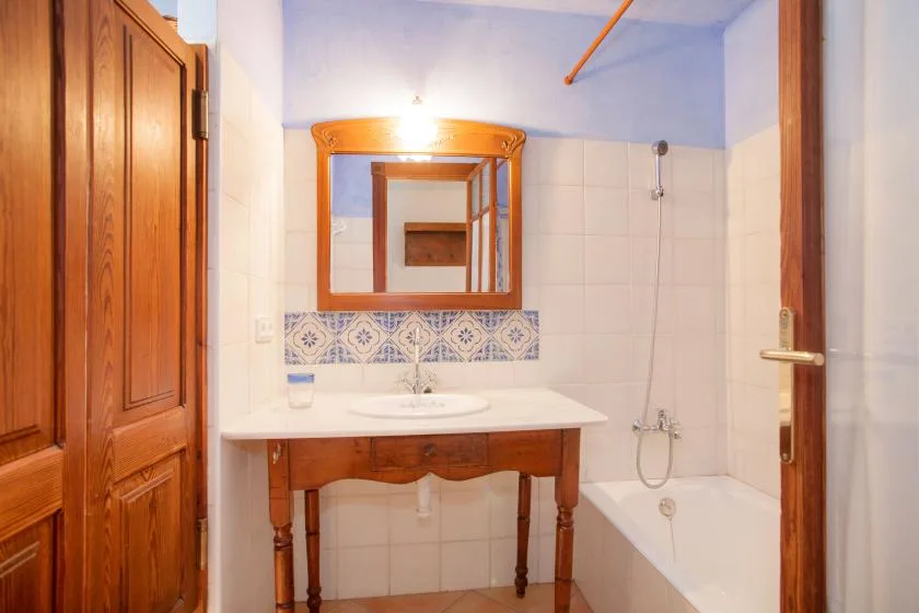 A tiled bathroom with a wooden vanity, mirror, and bathtub.