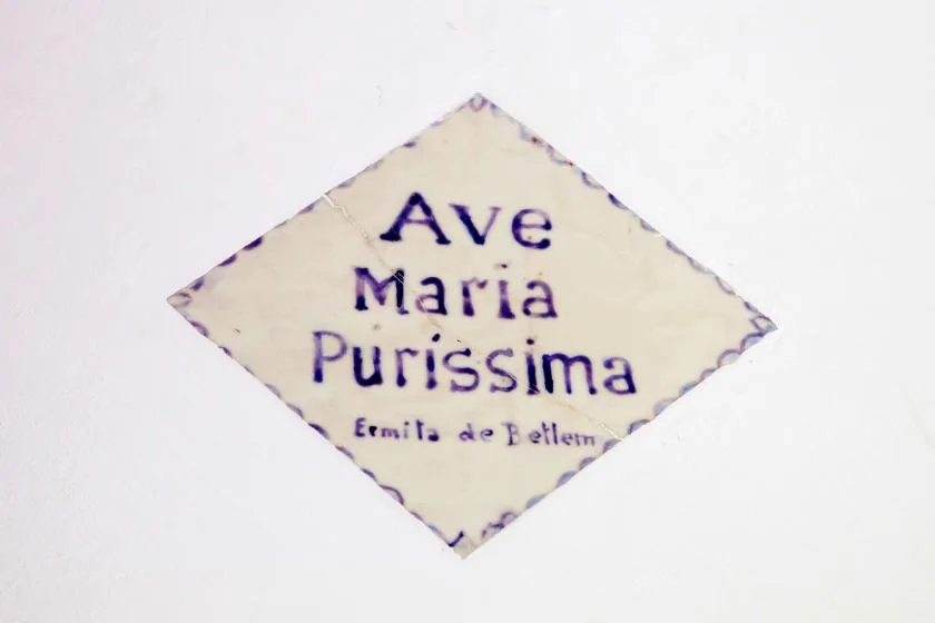 A diamond-shaped religious sign with purple lettering is mounted on a white wall.