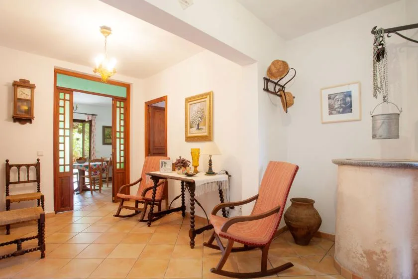 A tiled sitting room with wooden seating and a dining area visible through the doorway.